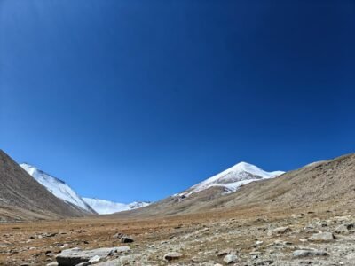 Barren rocky plain with snow-capped mountains under a clear blue sky.